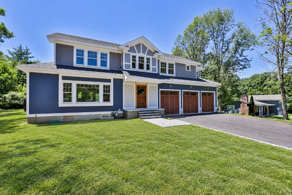 Blue-gray custom home with a finished lawn, wood front door, and three-car garage in Amesbury, Massachusetts